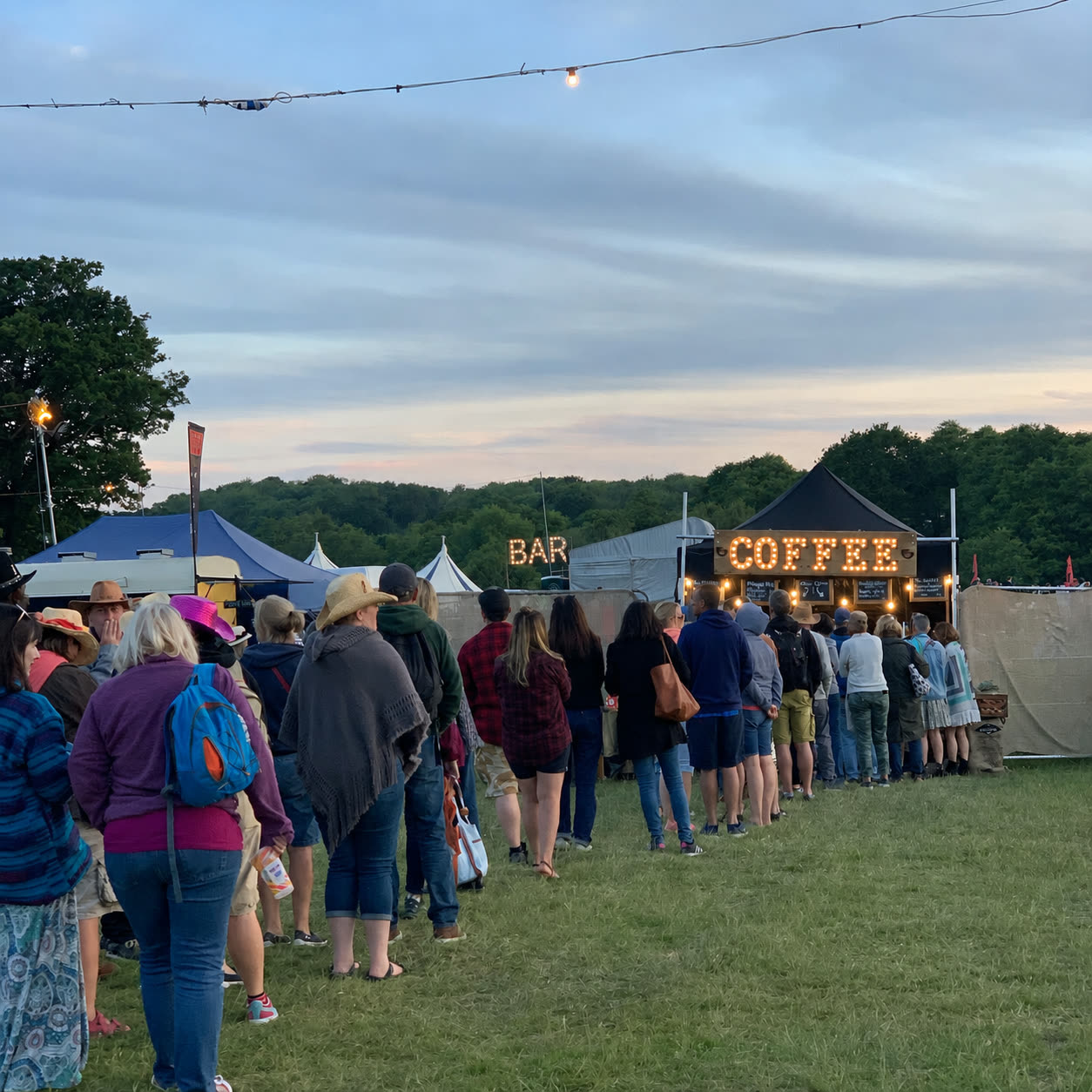 Queue of festival-goers at the Fine Grind COFFEE marquee at dusk under festoon lights